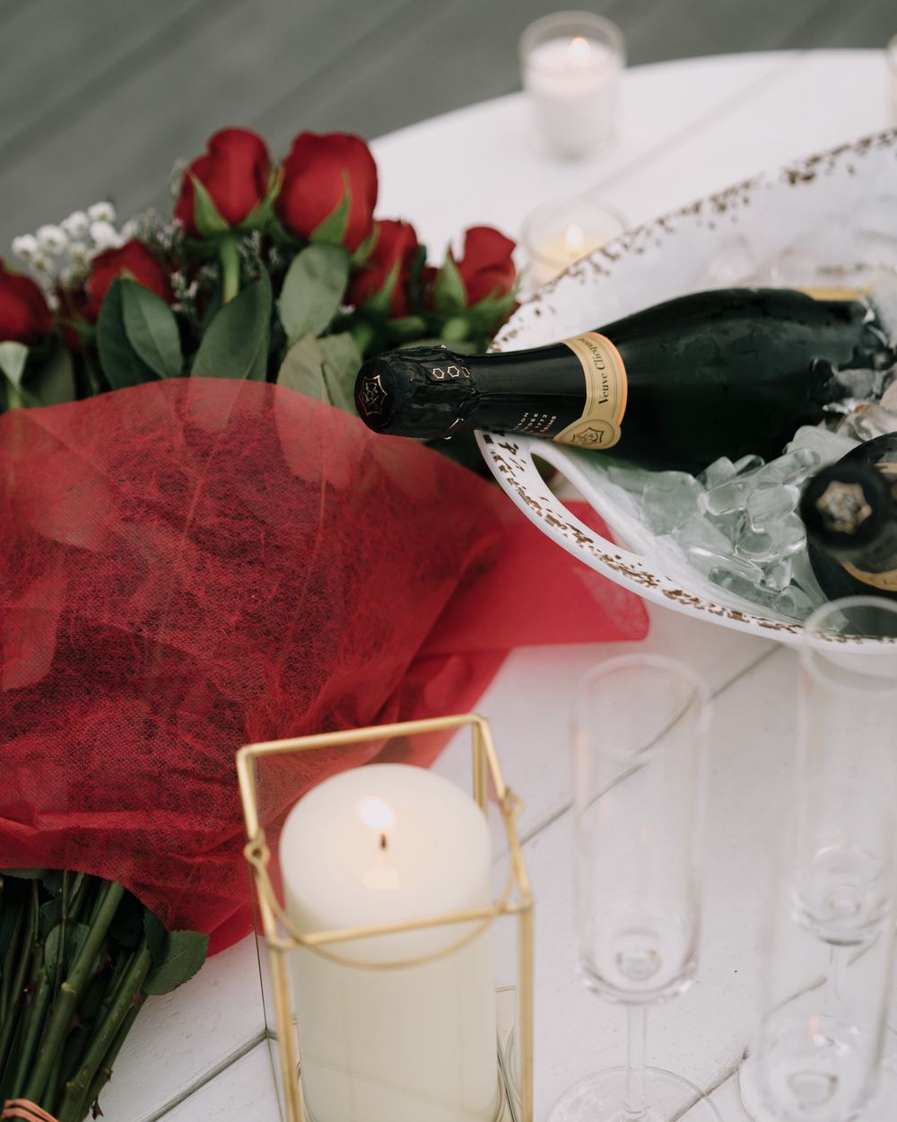 Red roses and white candles arranged with champagne bottles on an elegant table setting.