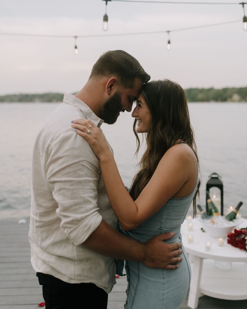 A couple embraces on a dock with a romantic lakeside setting at dusk.
