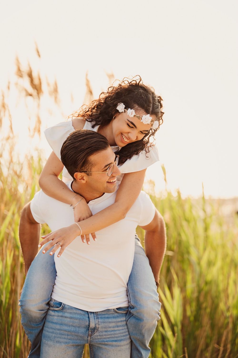 A playful piggyback ride outdoors with tall grass and golden sunlight creating a romantic summer moment.