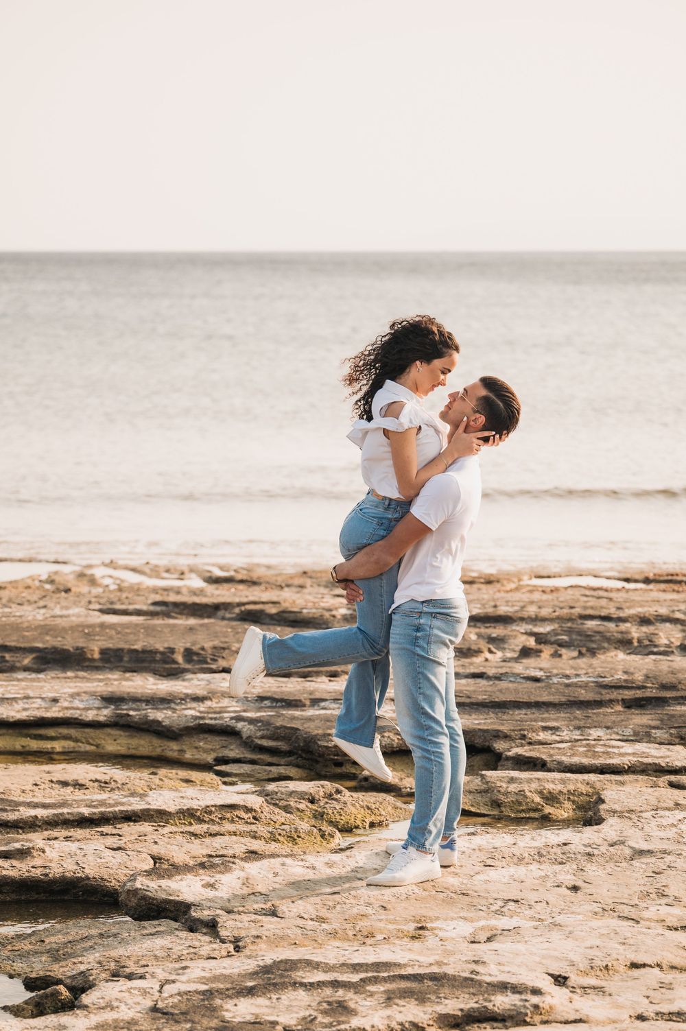 A joyful couple embracing on rocky coastal terrain with ocean waves in the background.