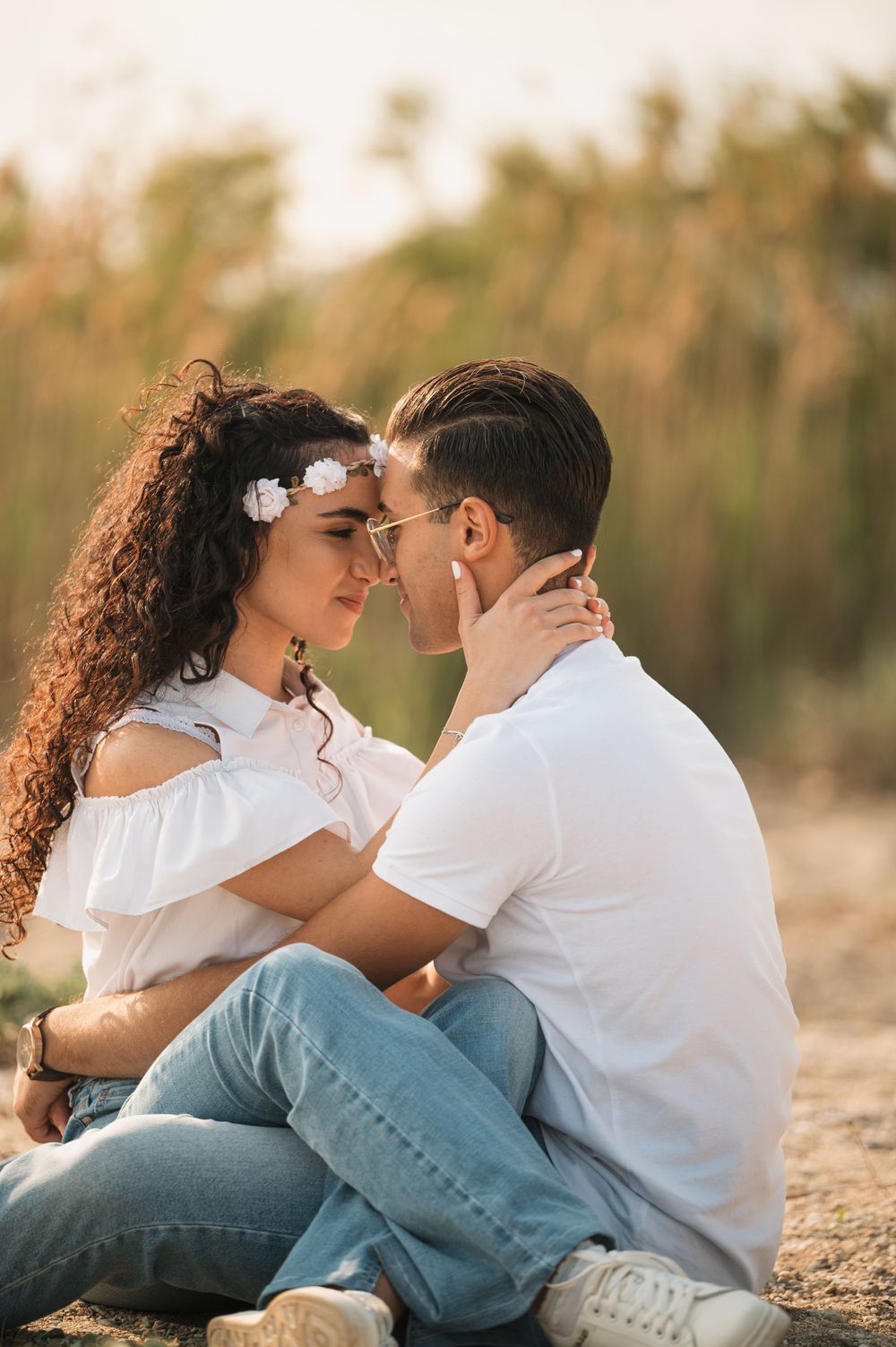 Romantic couple in white outfits embracing on beach during golden hour.