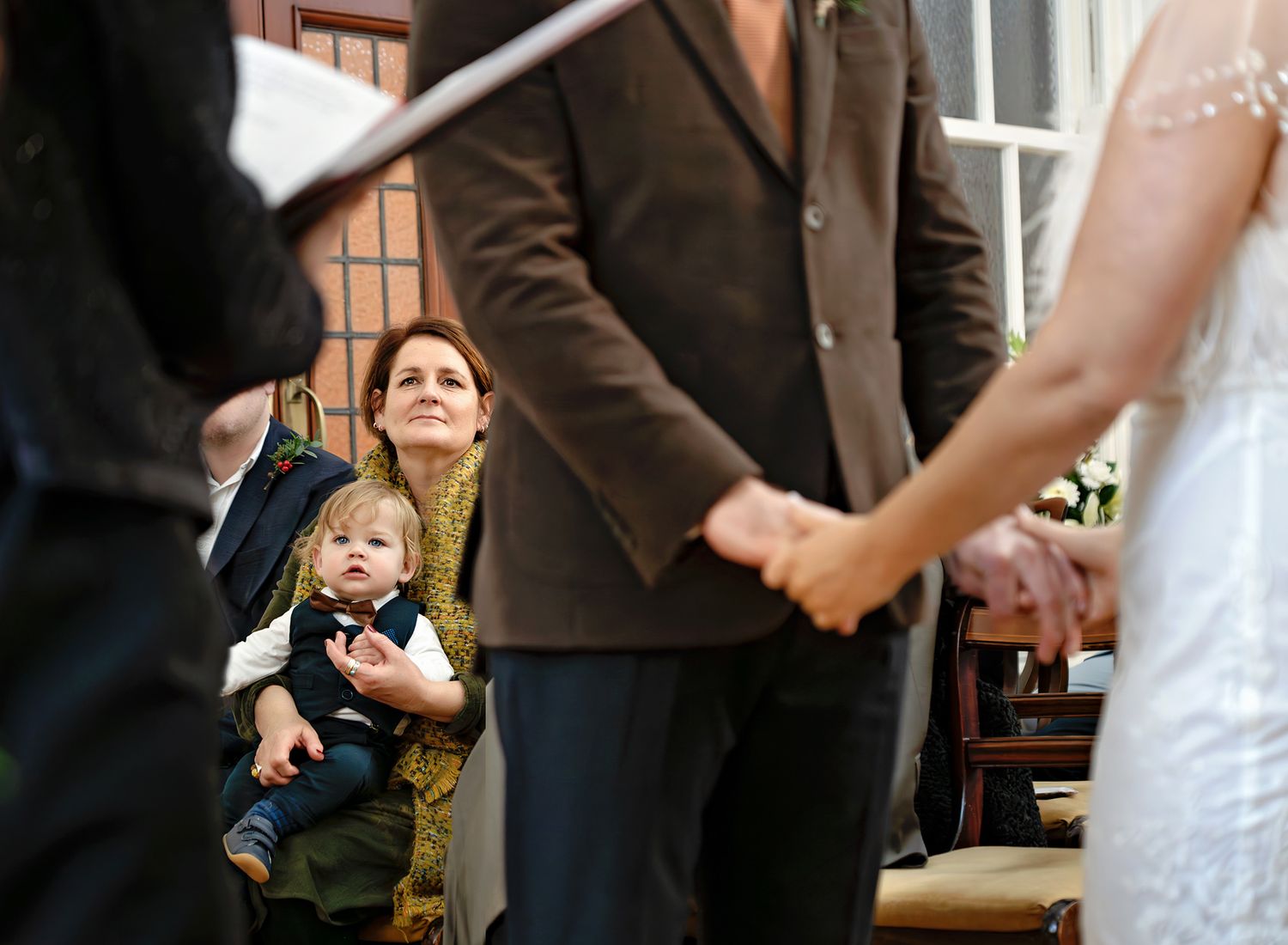 The bride and the groom are holding hands, and the focus is on their child, at a wedding ceremony in Bournemouth.