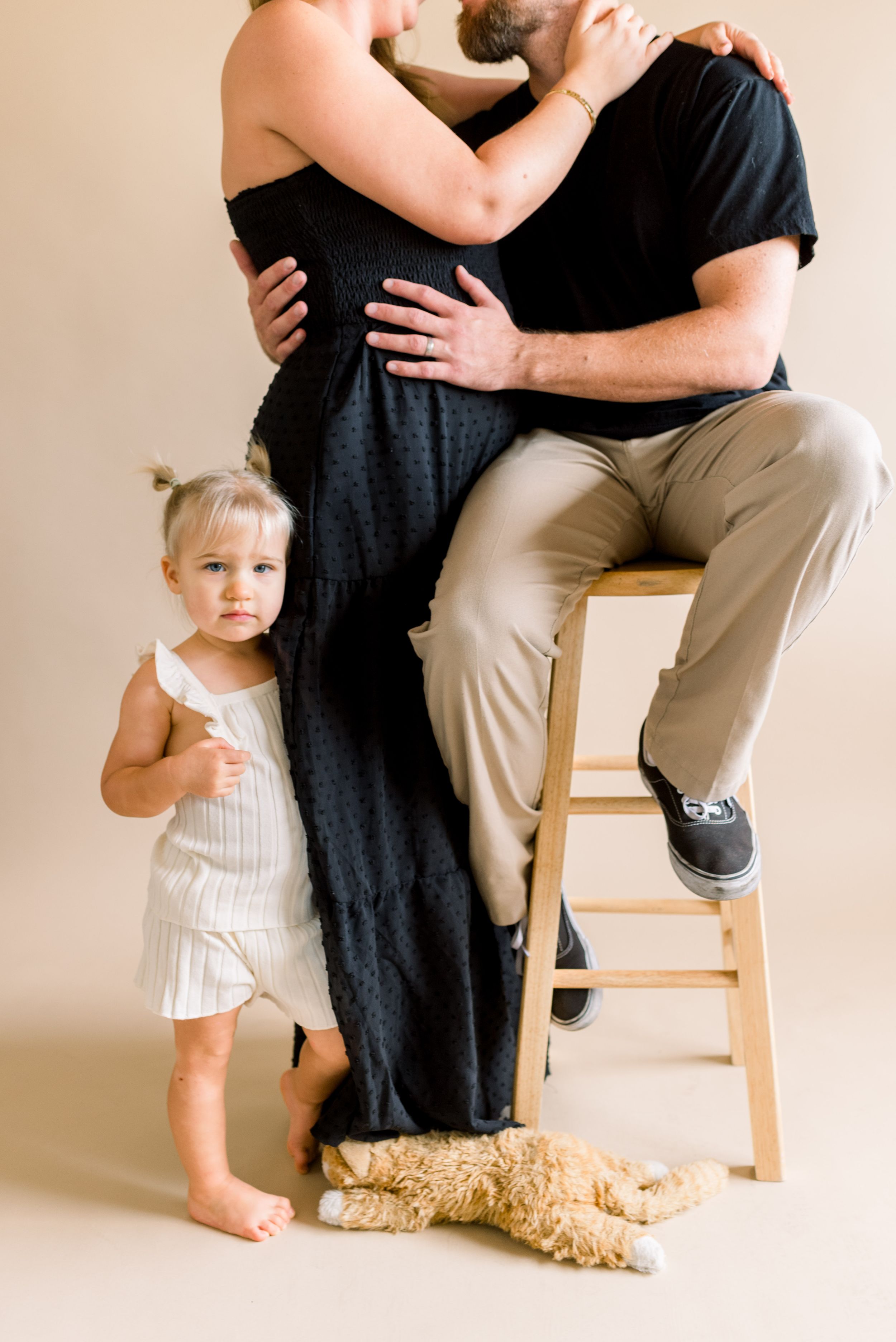 Family portrait with child standing beside parents and teddy bear on floor.