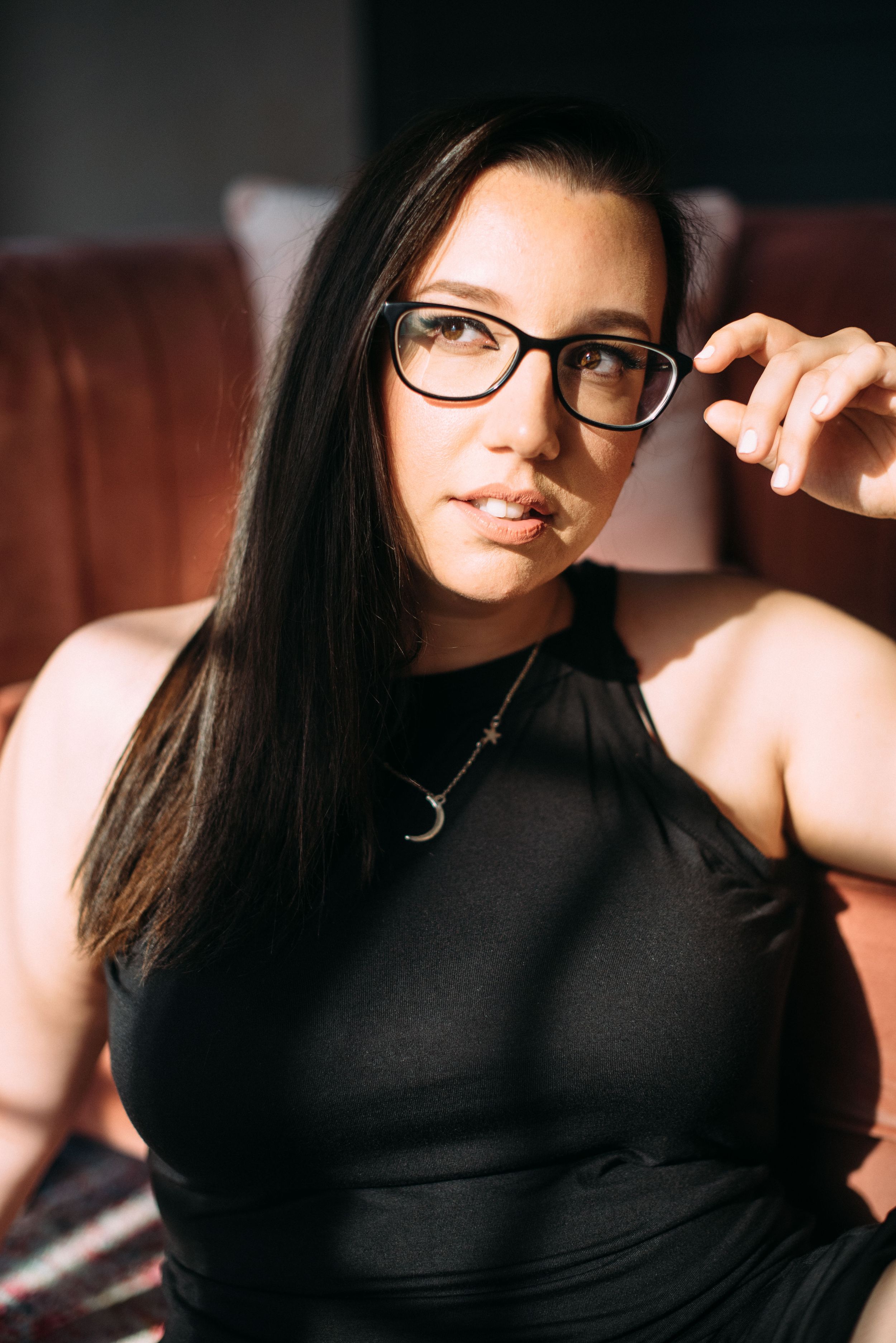 Portrait of a woman in black sleeveless top and glasses in warm lighting.