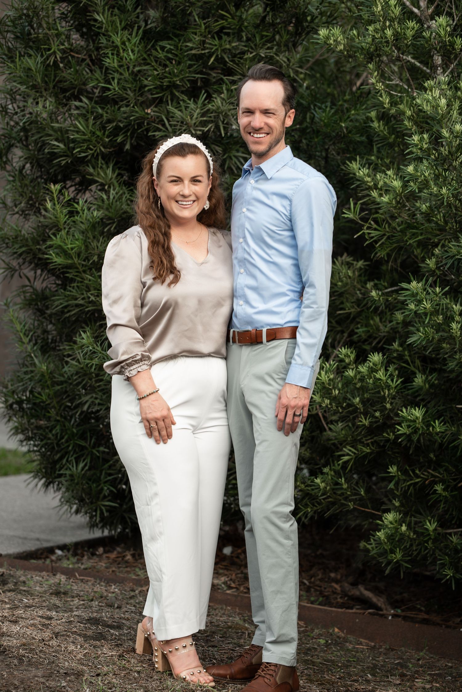 Casual couple posing together against green foliage background.