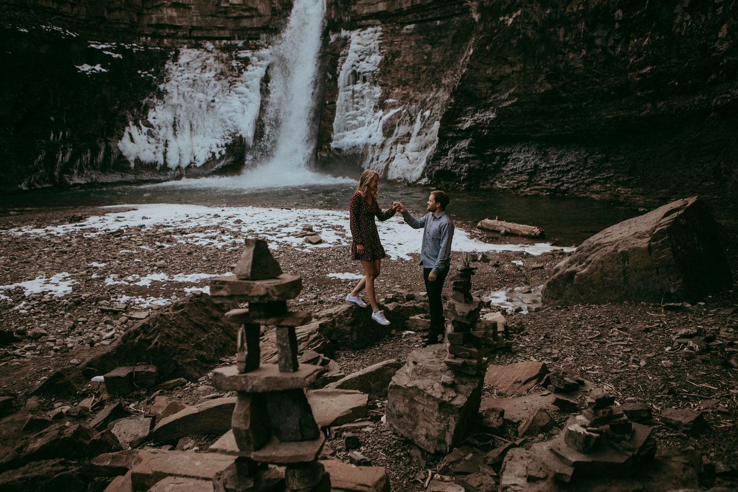 Three photographers capturing scenic waterfall shots from rocky terrain.