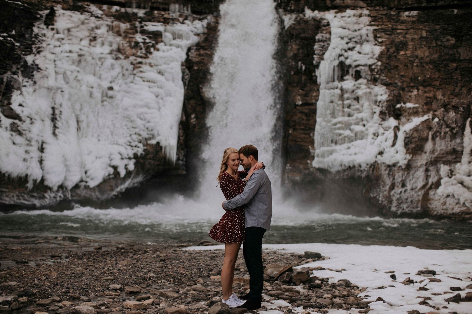 A romantic couple embracing in front of a majestic waterfall cascading down rocky cliffs.