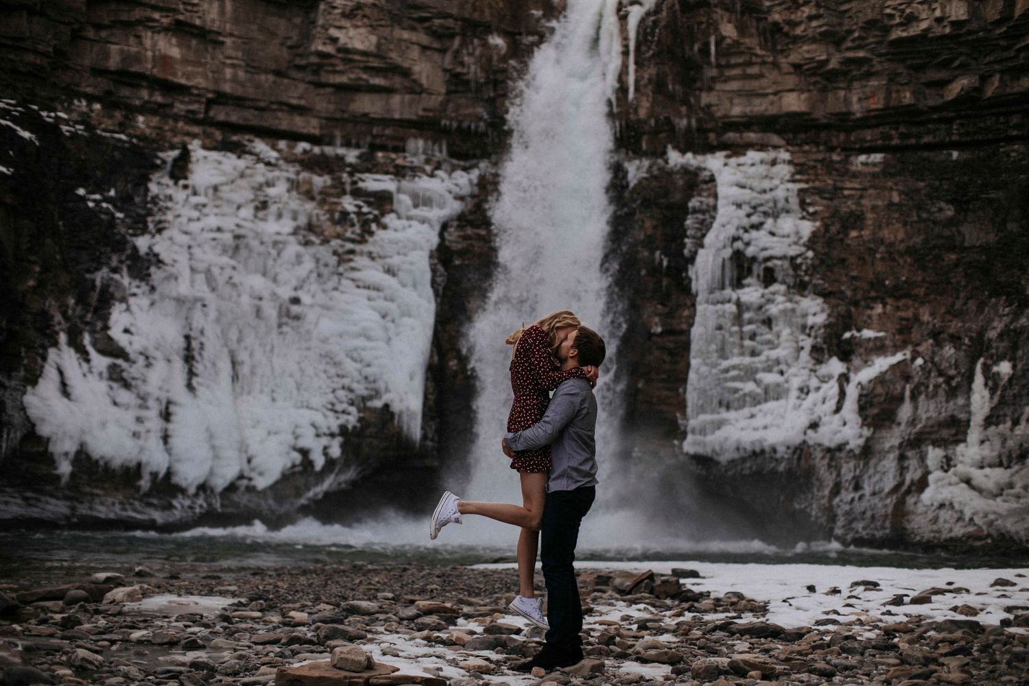 Intimate embrace captured in silhouette against dramatic waterfall backdrop.
