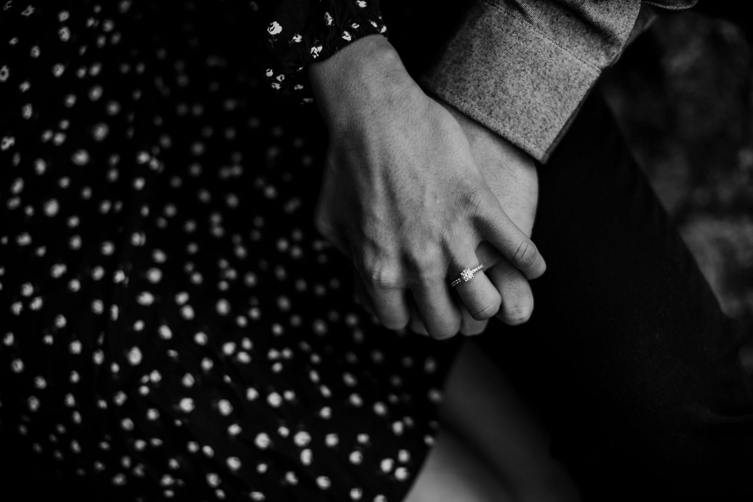 Close-up black and white shot of hands clasped together against a polka dot dress.