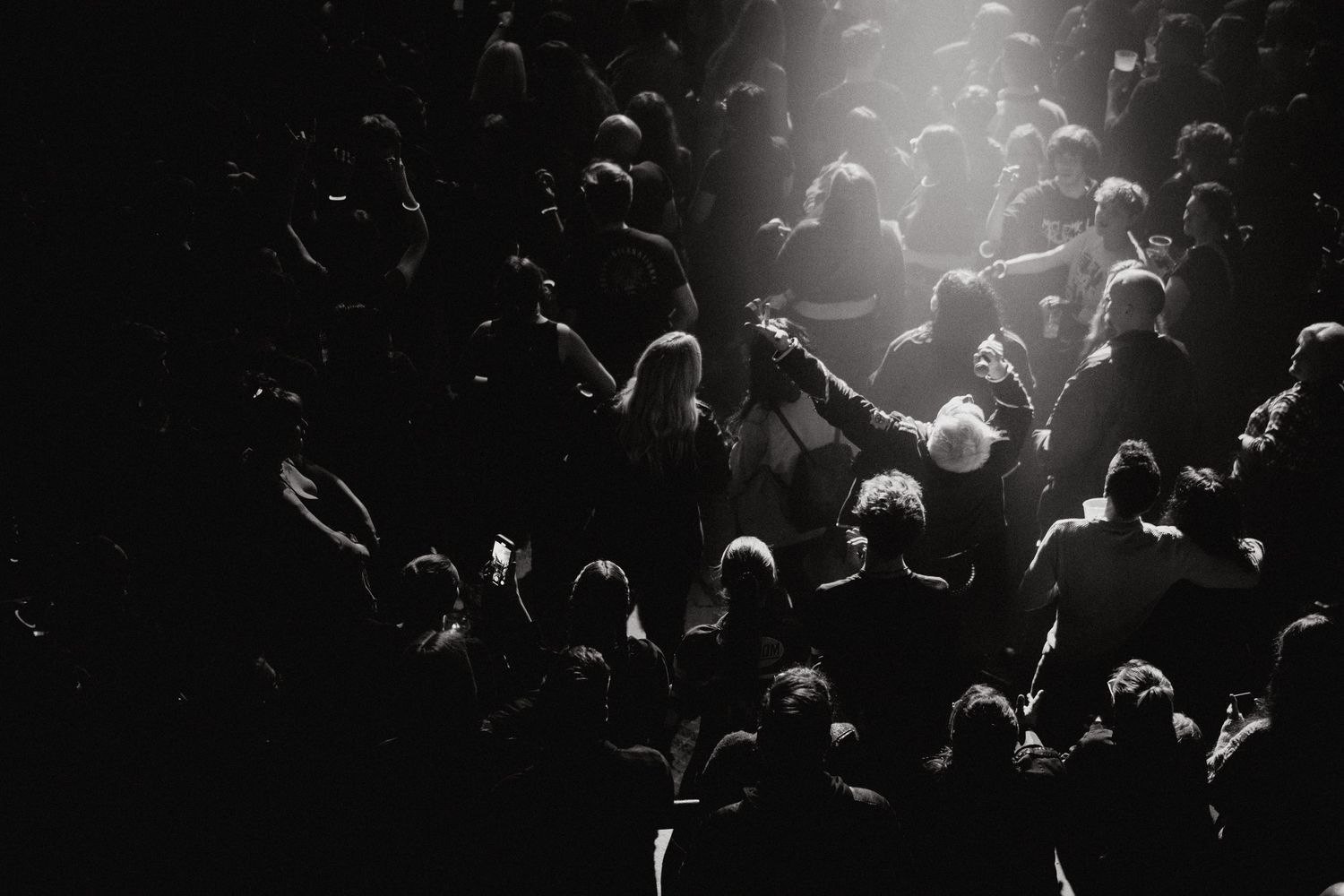 Dramatic concert crowd silhouettes illuminated from above by bright stage lights during a live performance.