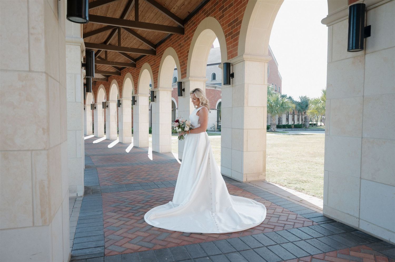 Elegant white wedding gown photographed under a columned archway with brick details.