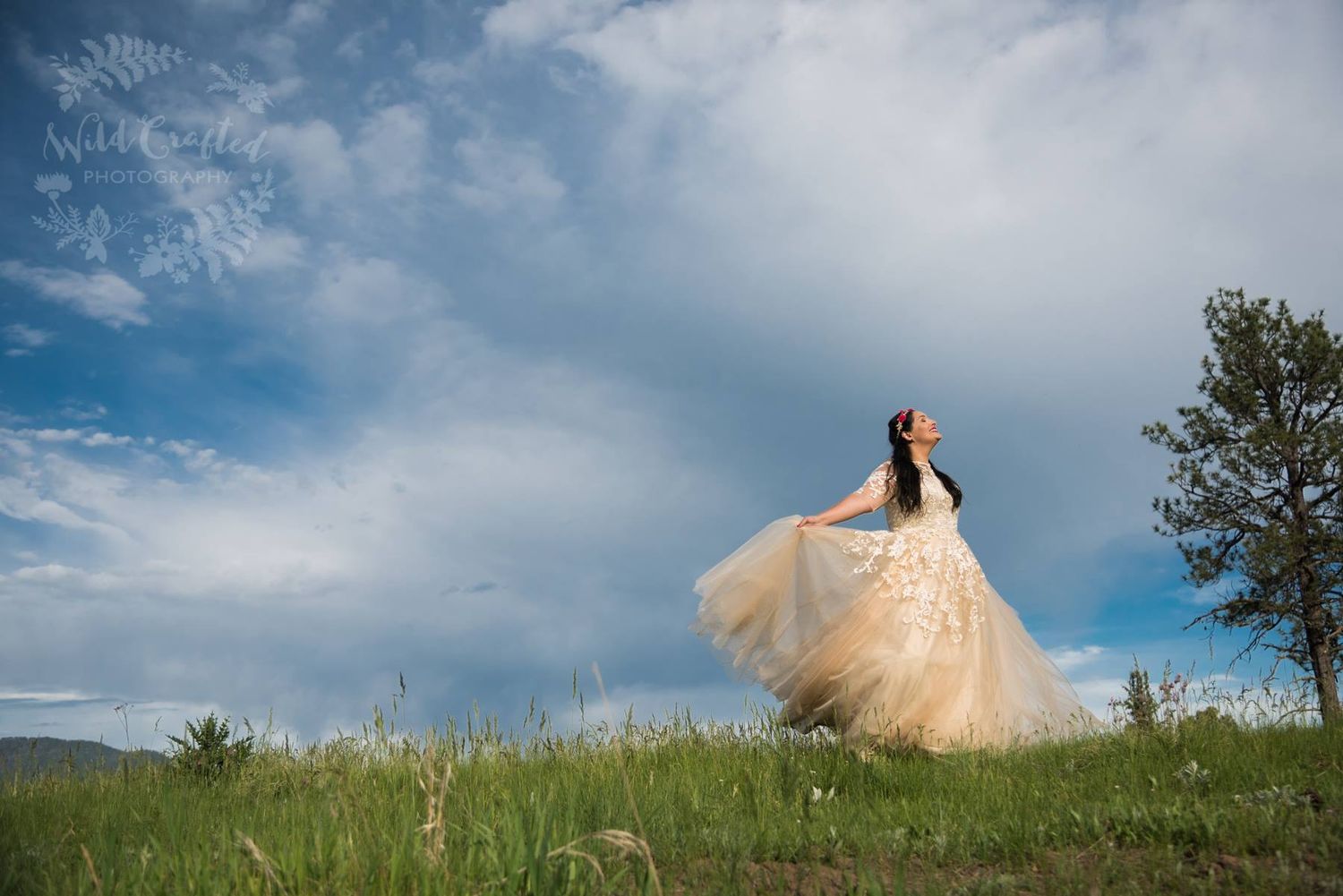 bride twirling on a lush green grassy hill with blue sky and clouds behind her