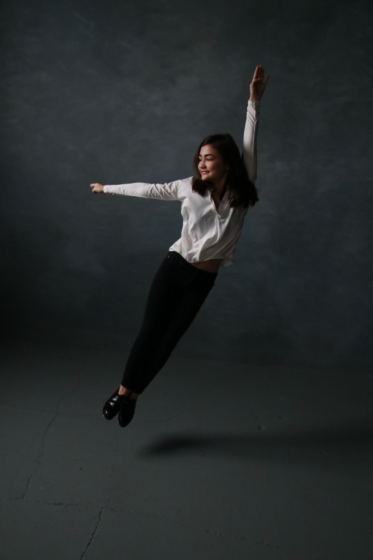 A dancer in white shirt and black pants leaps gracefully against a dark background.