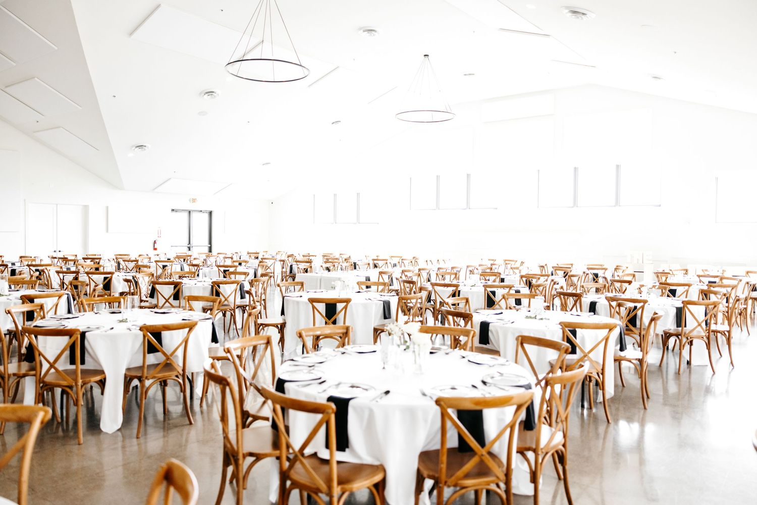 Elegant reception hall set with cross-back chairs and round tables draped in white linens.