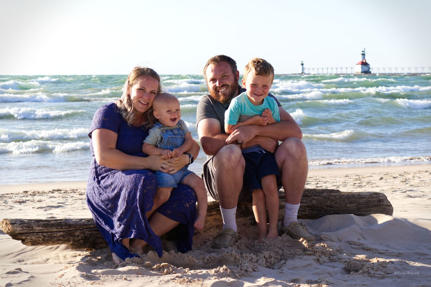 Family of four sitting on a log at Silver Beach, Lake Michigan. A lighthouse is in the background and waves are abundant