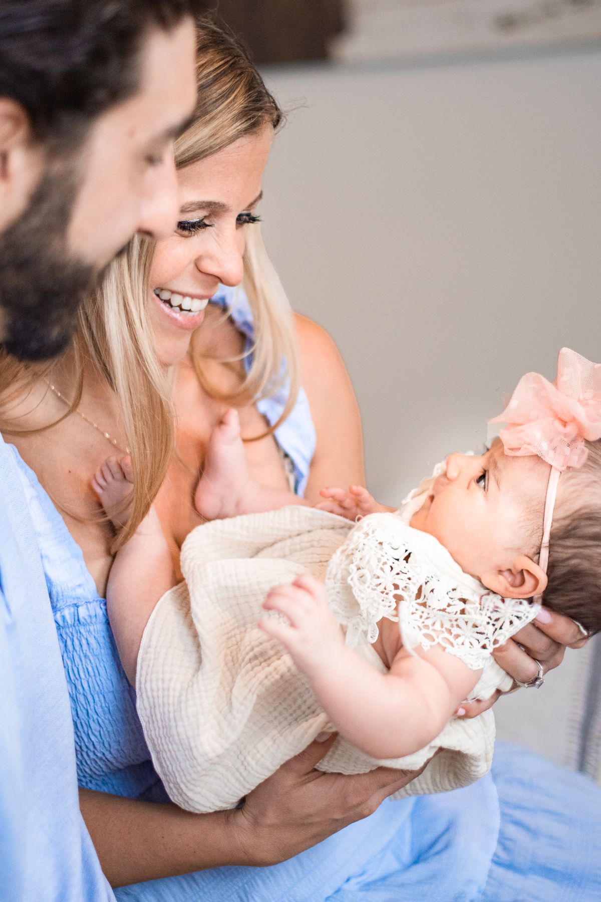 mother and father holding a baby girl in a pink bow for her newborn photoshoot.