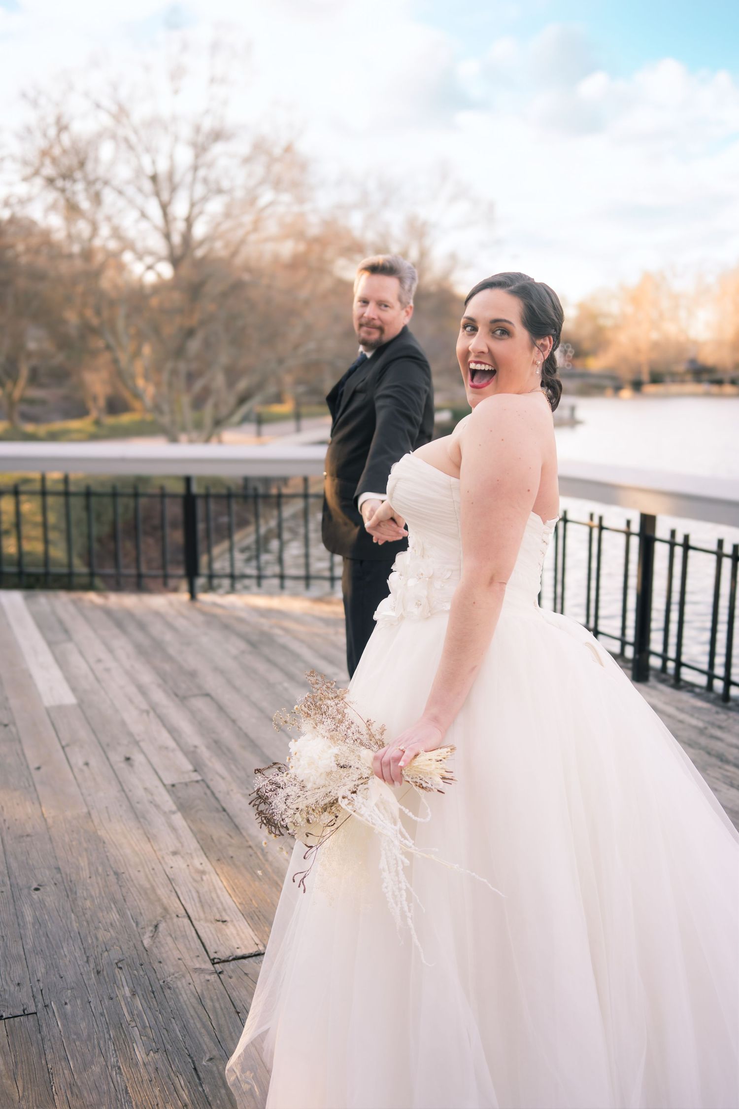 A bride in a white ballgown poses on a wooden deck during an outdoor photoshoot.