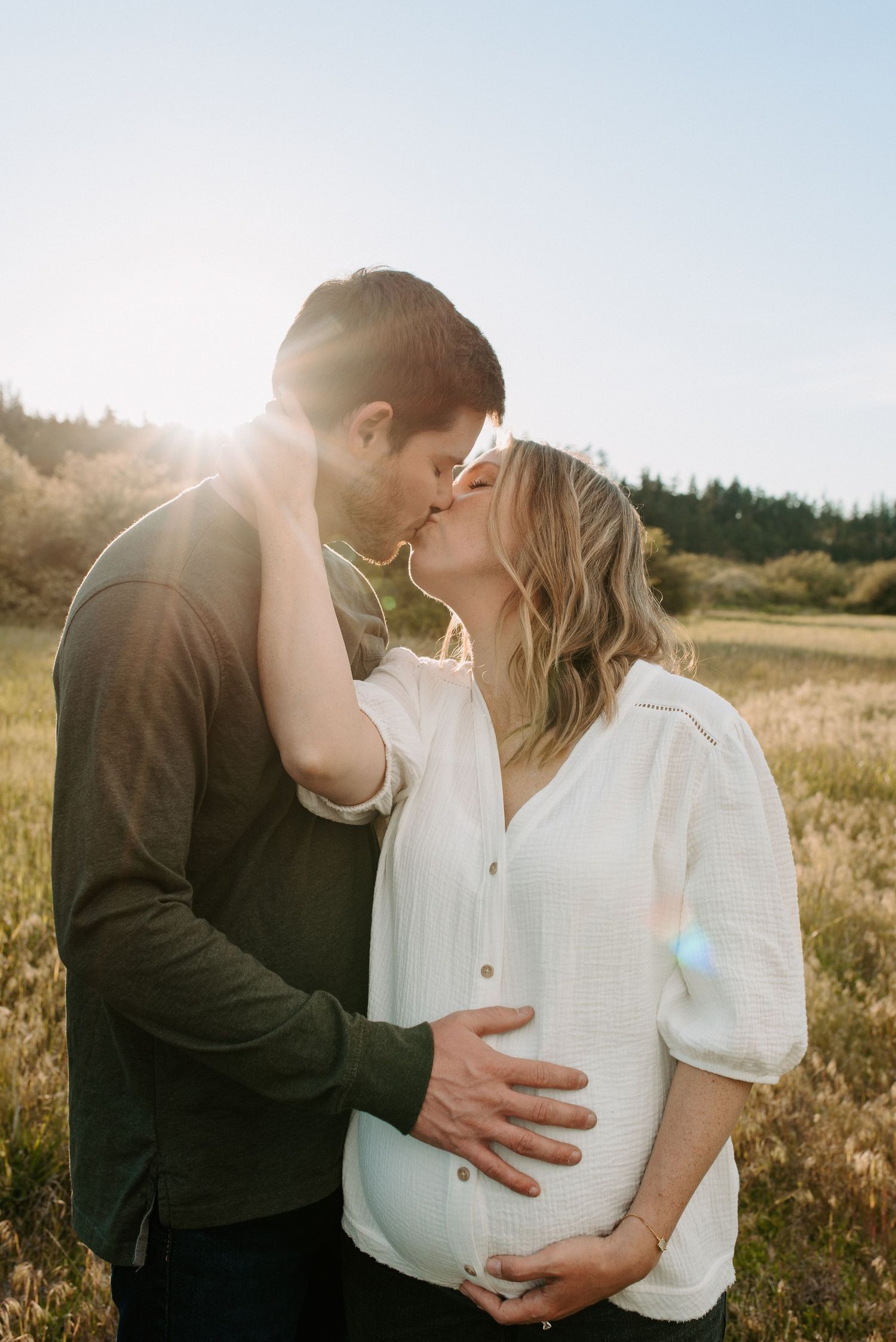 Romantic couple embracing in sunlit field during golden hour photoshoot.