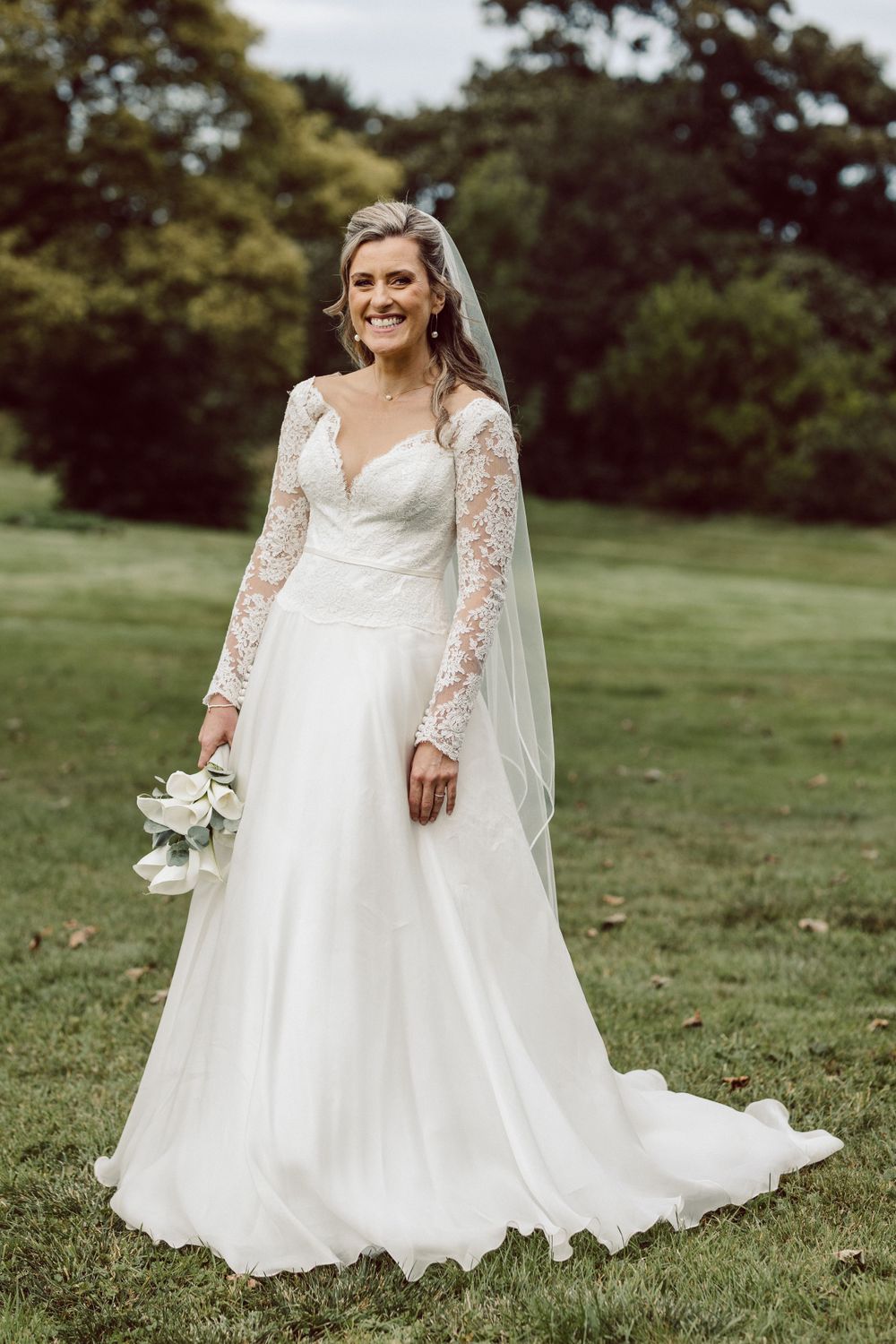 Beautiful wedding dress with lace sleeves and flowing skirt captured in outdoor garden setting.