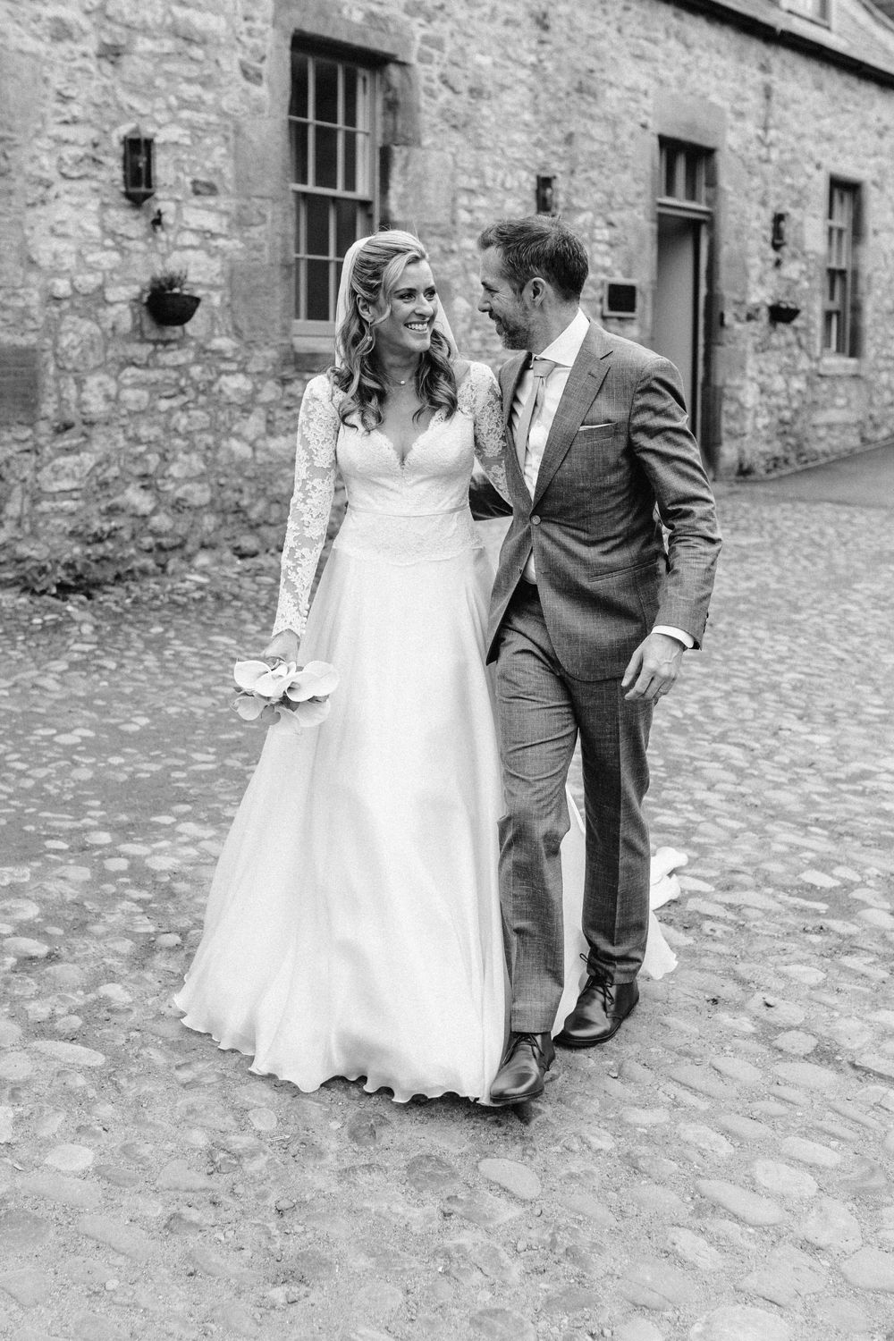 Black and white series of newlyweds walking together on cobblestone courtyard.