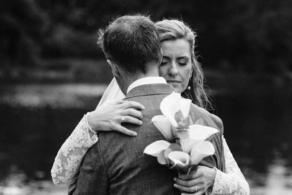 Black and white romantic portrait of couple embracing by the water.