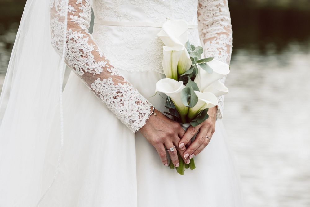 Close-up of bride's lace detailed dress sleeves and white floral bouquet.