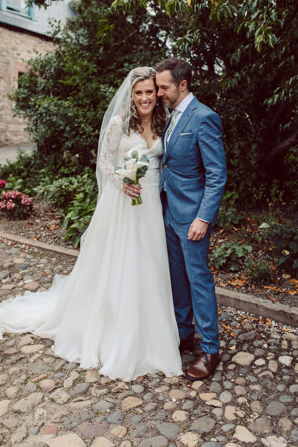 Wedding couple shares intimate moment on cobblestone path by historic stone building.