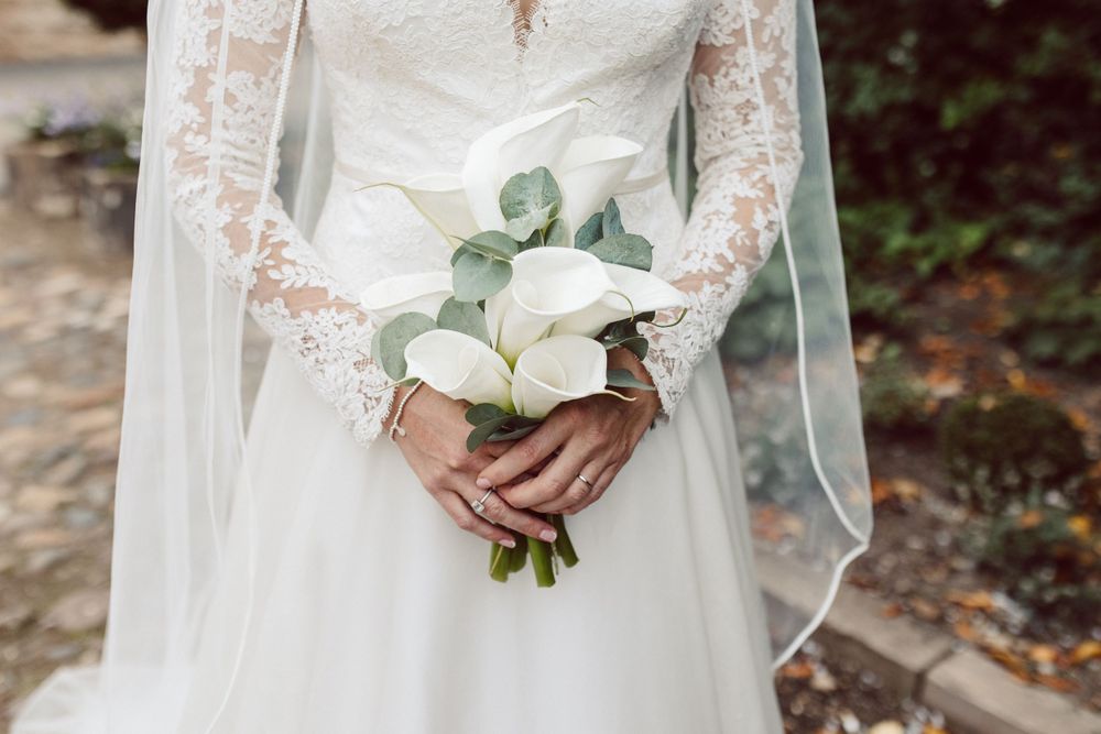 Close-up details of white lace wedding dress and bouquet against stone background.