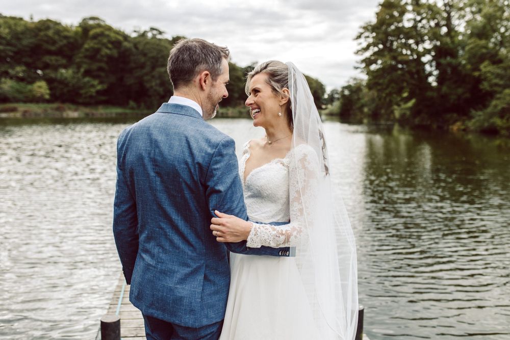 Newlyweds standing close together on lakeside dock during wedding photoshoot.