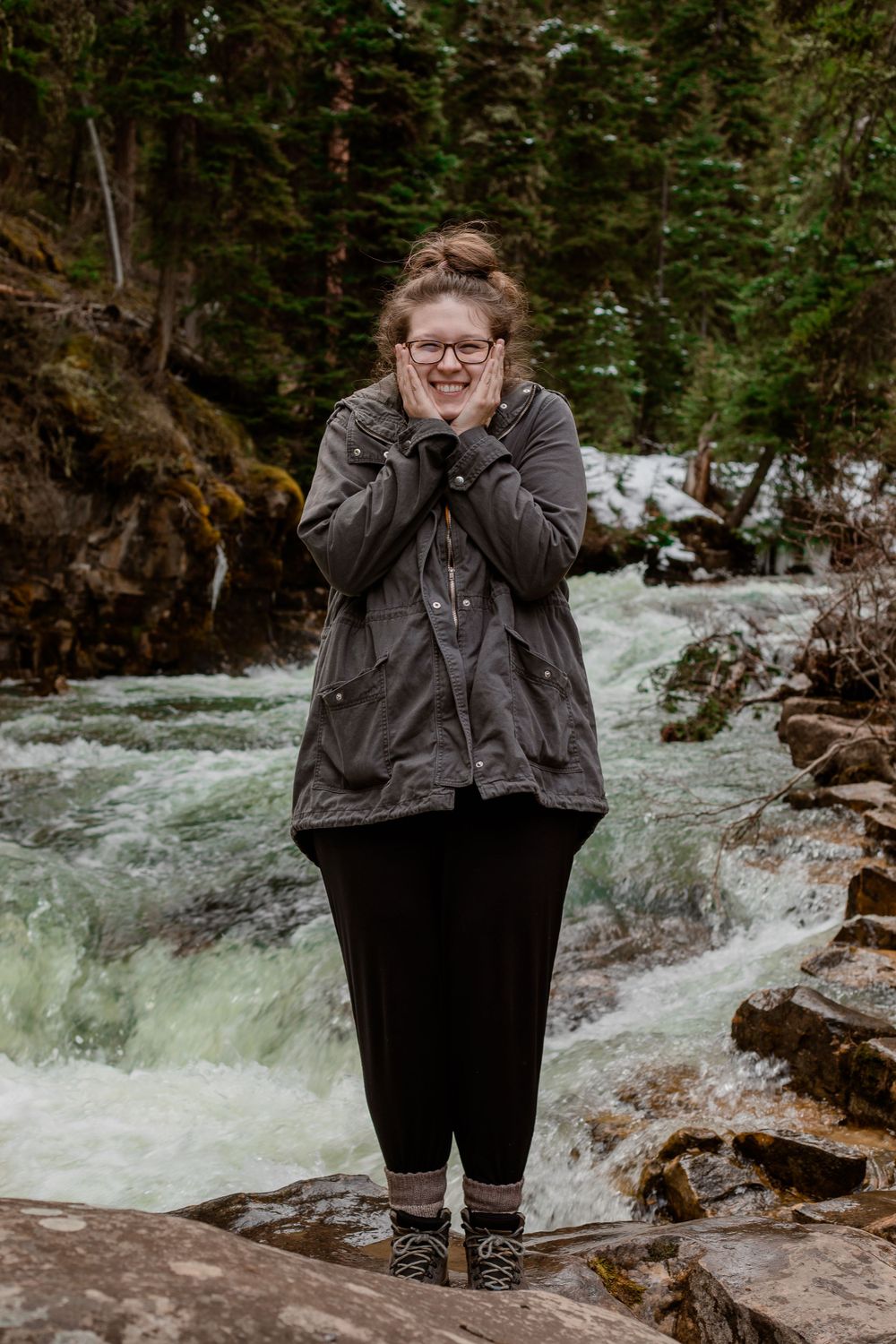 Raimi Ellen holding her hands to her face as she smiles at the camera in front of a River feature in Montana