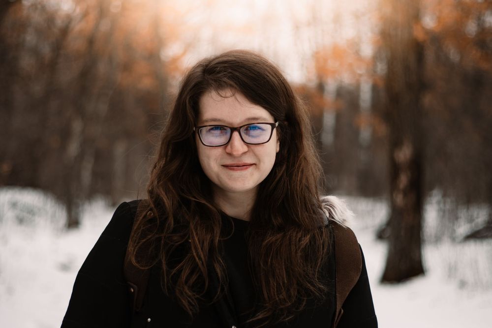 Raimi Ellen smiling at the camera as she walks on a snow covered trail with fall leaves still on trees