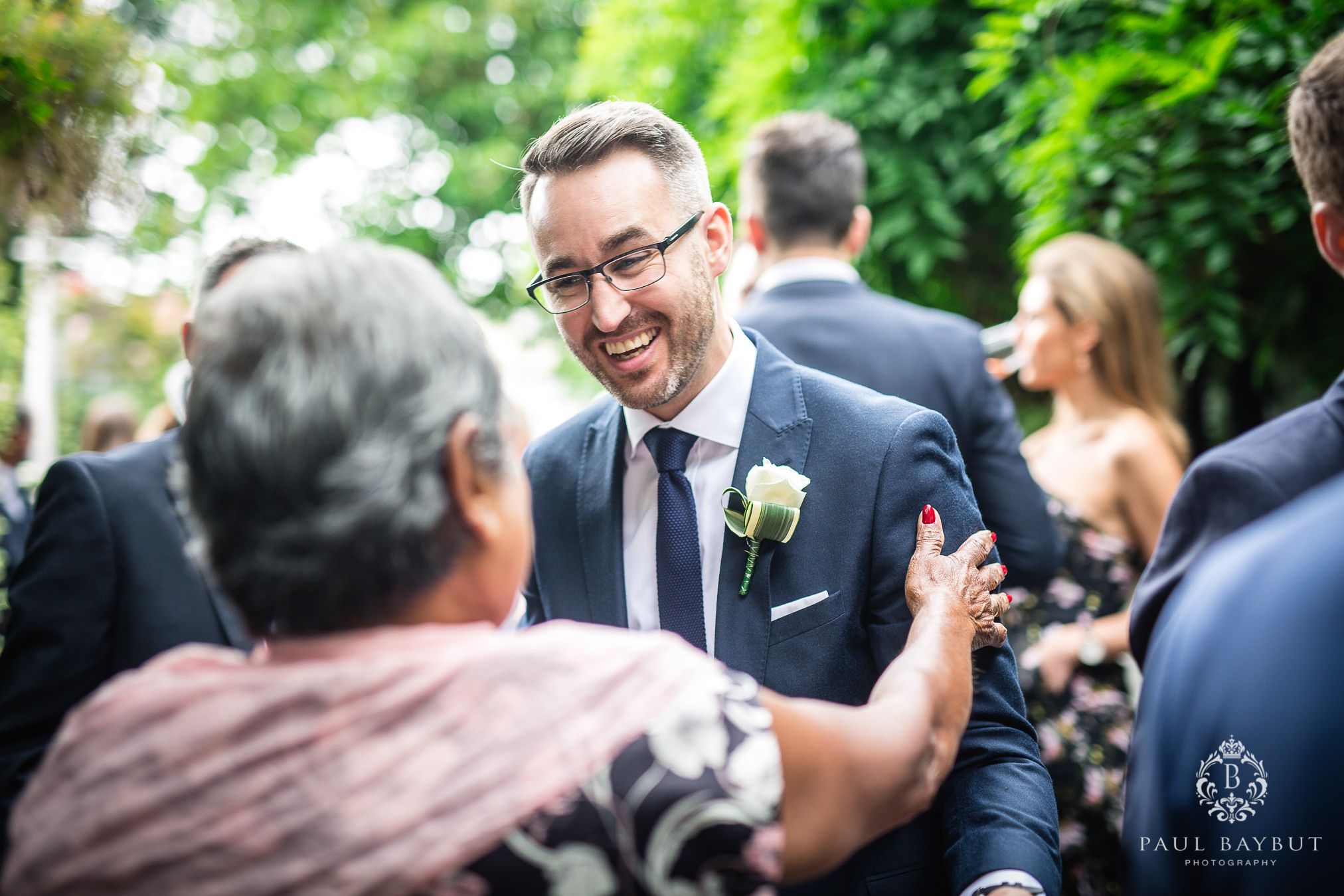 Wedding guest in suit and glasses sharing a laugh at outdoor reception.