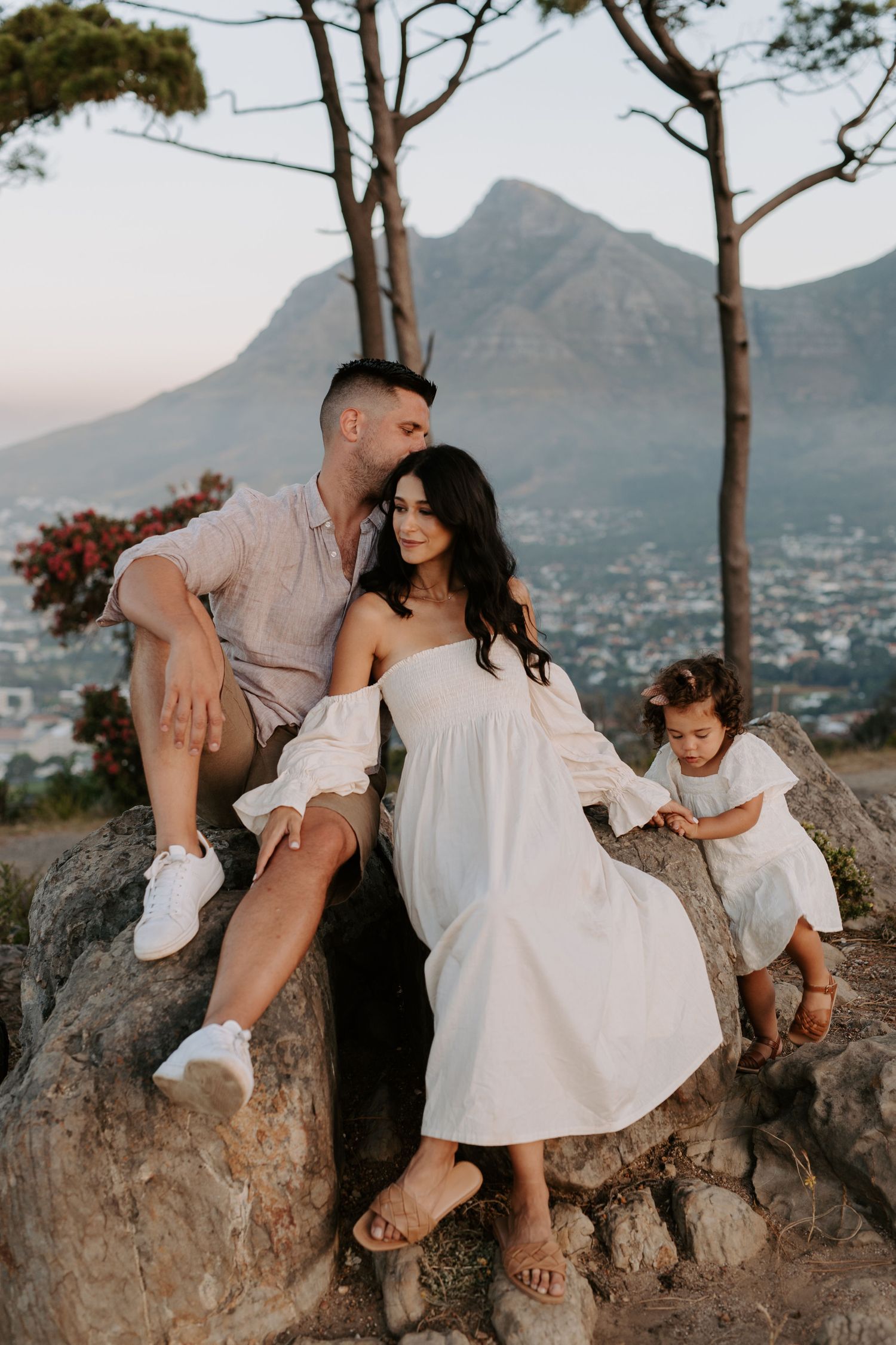 A family poses together on rocky terrain with a majestic mountain peak in the background during sunset.