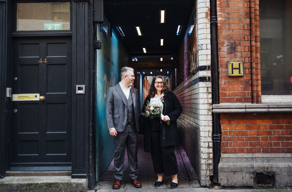 A couple stands in an urban doorway with brick walls and modern lighting.