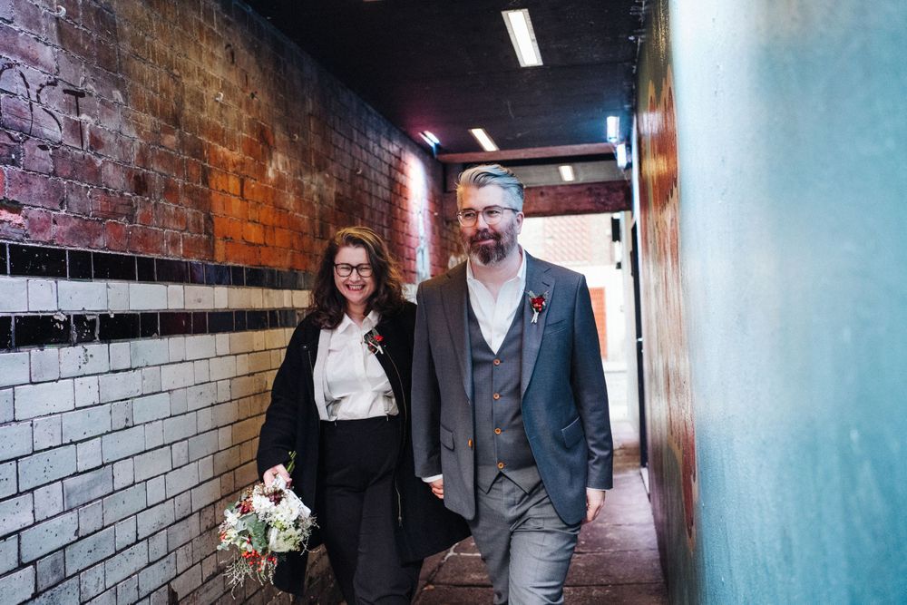 A couple walks through an industrial-style hallway with exposed brick walls.