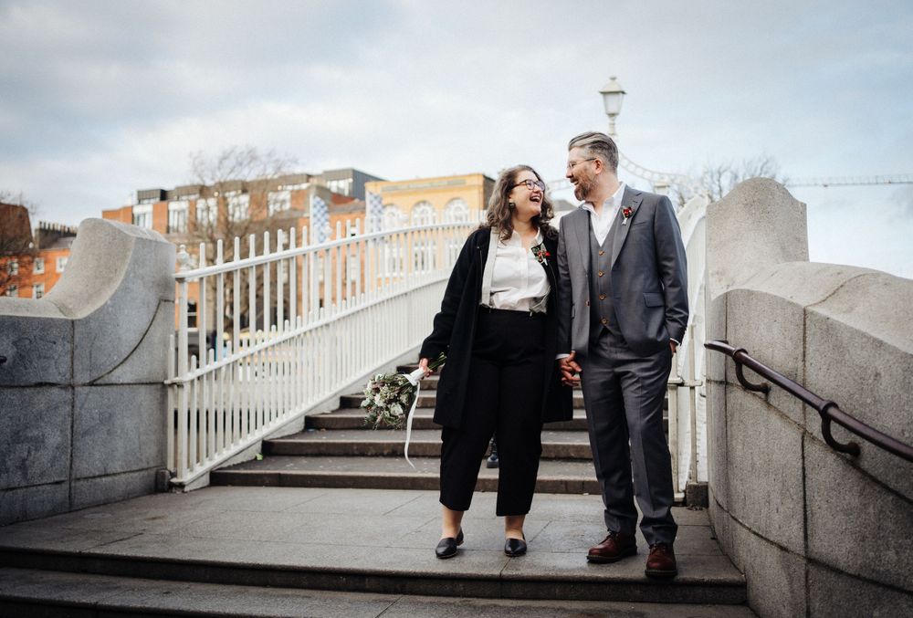 A couple walks down stone steps together with city buildings visible in the background.