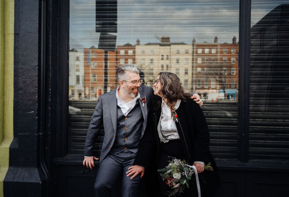 A couple shares an intimate moment on a bench with classic architecture in the background.