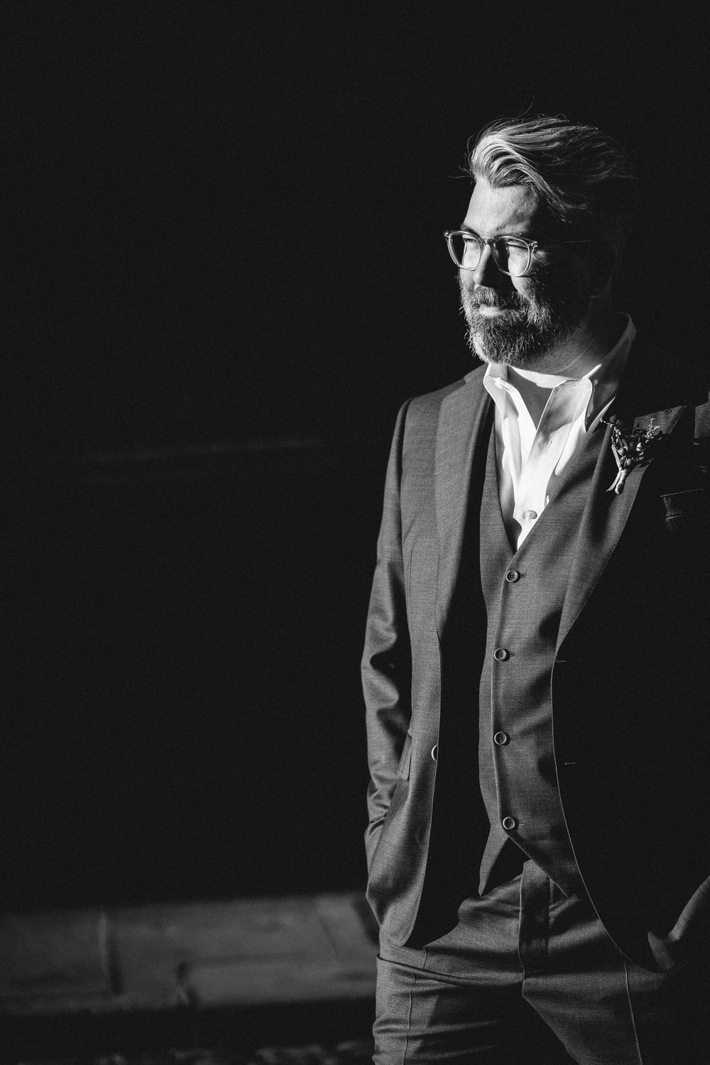 A dramatic black and white portrait of a person in formal attire against a dark background.