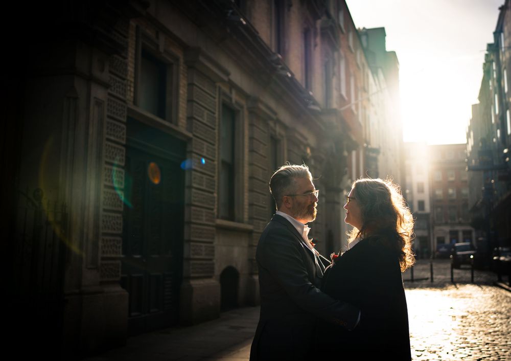 A couple embraces in golden sunlight on an urban street with historic architecture.