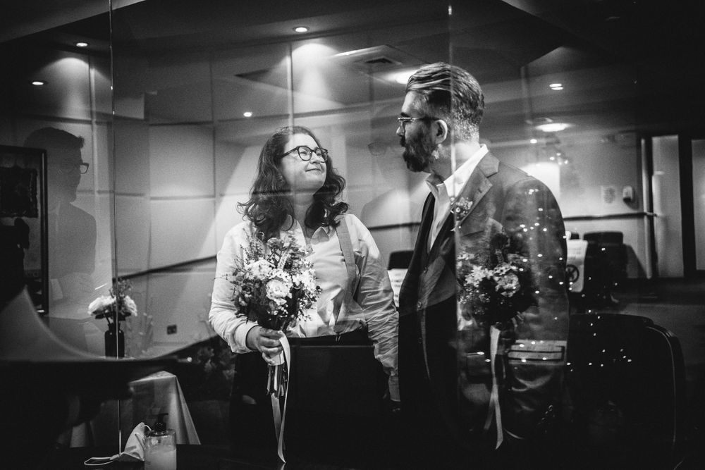 A couple shares an intimate moment while holding a bouquet in a dimly lit indoor space.