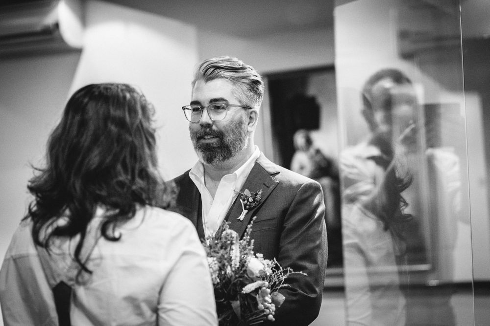 A couple shares a tender moment in front of a mirror during what appears to be a wedding ceremony.