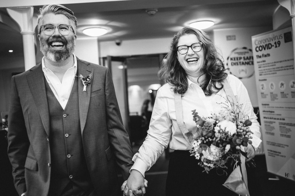 A happy couple walks down a hallway holding hands with a COVID-19 sign visible.