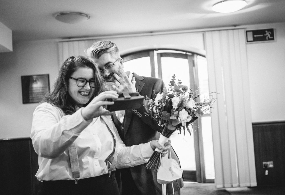 A couple looks at something on a mobile phone while holding a floral bouquet.