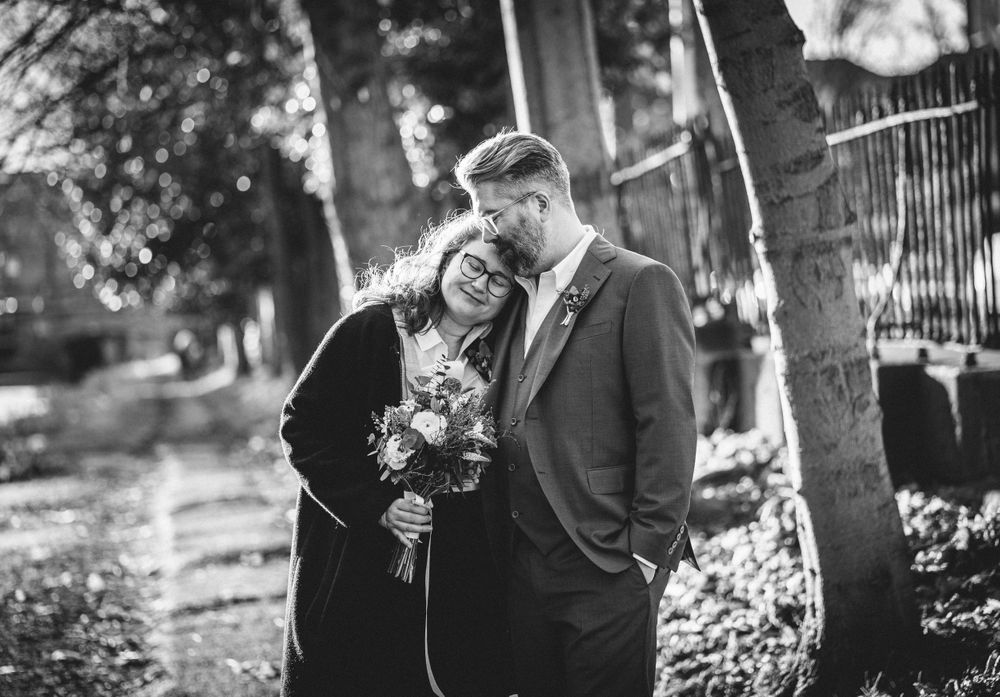 A tender black and white portrait of a couple embracing outdoors among trees.