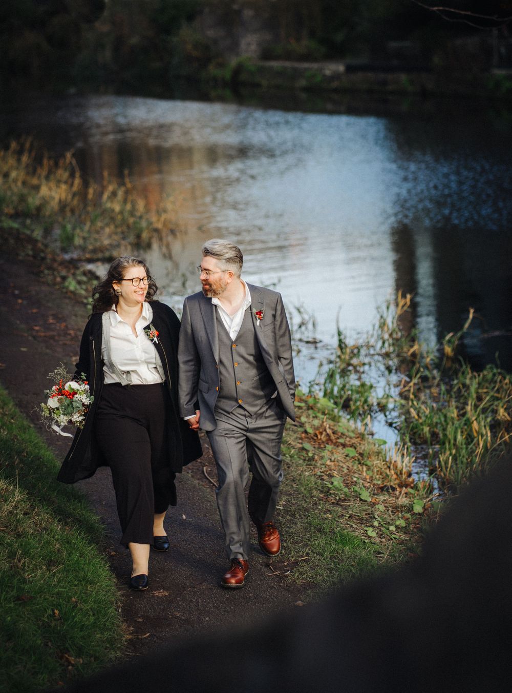 A couple walks together on a scenic path alongside a tranquil pond.