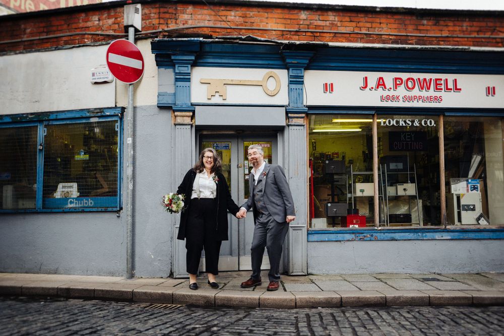 A couple stands in front of a traditional storefront on a cobblestone street.