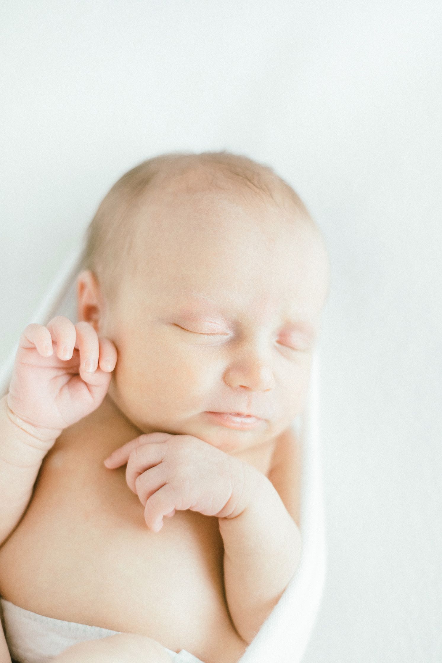 Sleeping baby photographed in dreamy high-key style against white background.