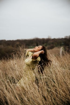 Woman in yellow dress posing dramatically in tall autumn grass field.