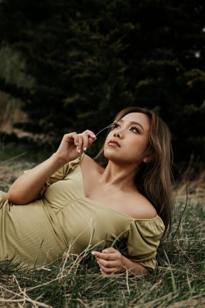 Portrait of woman in olive green off-shoulder dress lying in grass field.