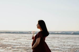 Maternity silhouette portrait of a woman in burgundy dress at beach during sunset.